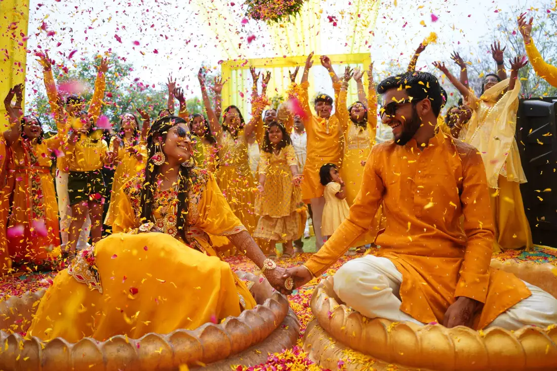A couple laughing at their haldi, under a shower of marigold and petals